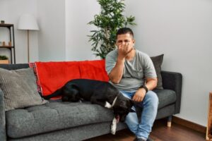 man lounging on the couch with his dog covering his nose due to foul AC smell