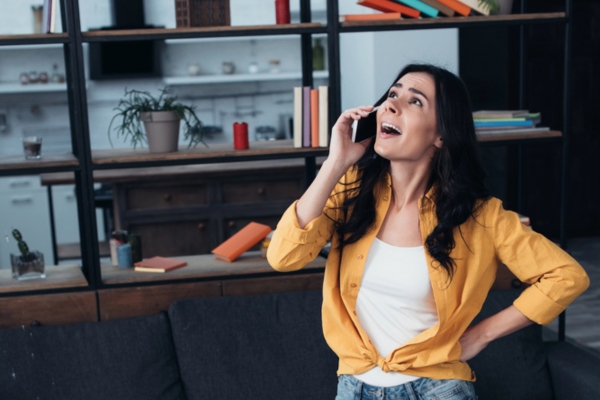 woman looking at home air conditioner that blows weak air while on the phone depicting calling HVAC company