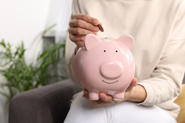 Woman putting coin into piggy bank at home depicting cost savings