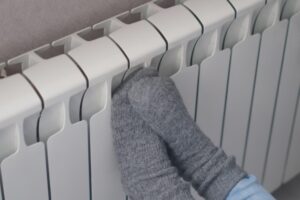 cropped view of a woman's feet with socks keeping warm in a radiator due to heating problems at home