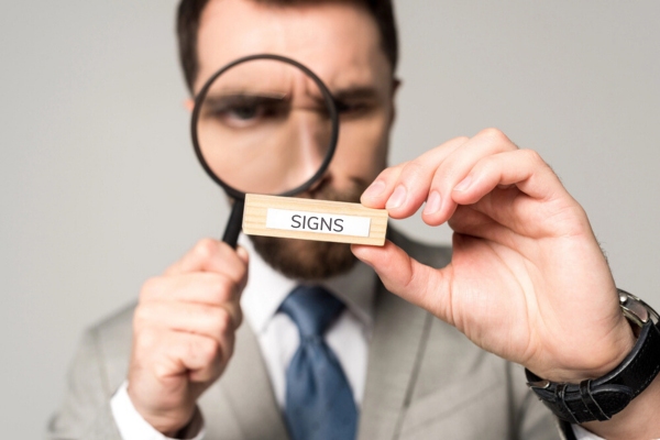 man using a magnifying glass looking at a wooden block with signs text depicting propane leaks