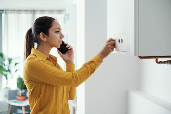 woman on the phone while looking at boiler depicting heating system breakdown